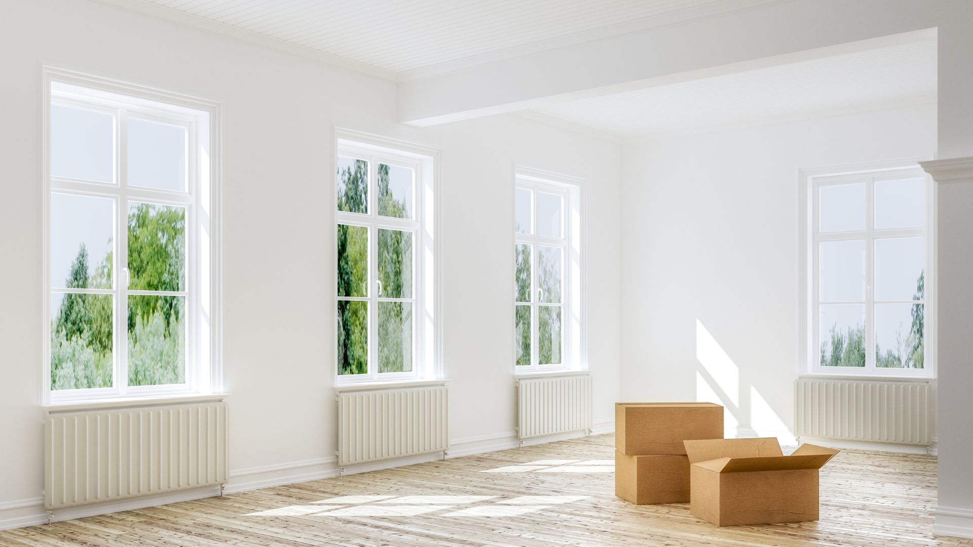 Empty room with large windows, wooden floor, and moving boxes