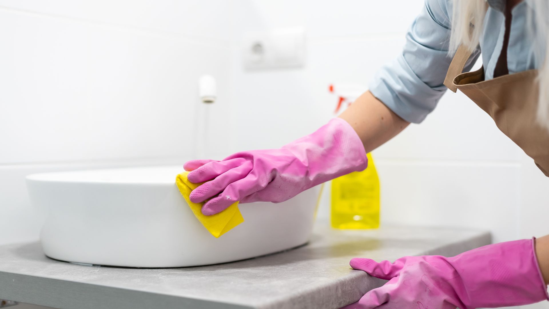 Pink gloves cleaning white sink with yellow cloth