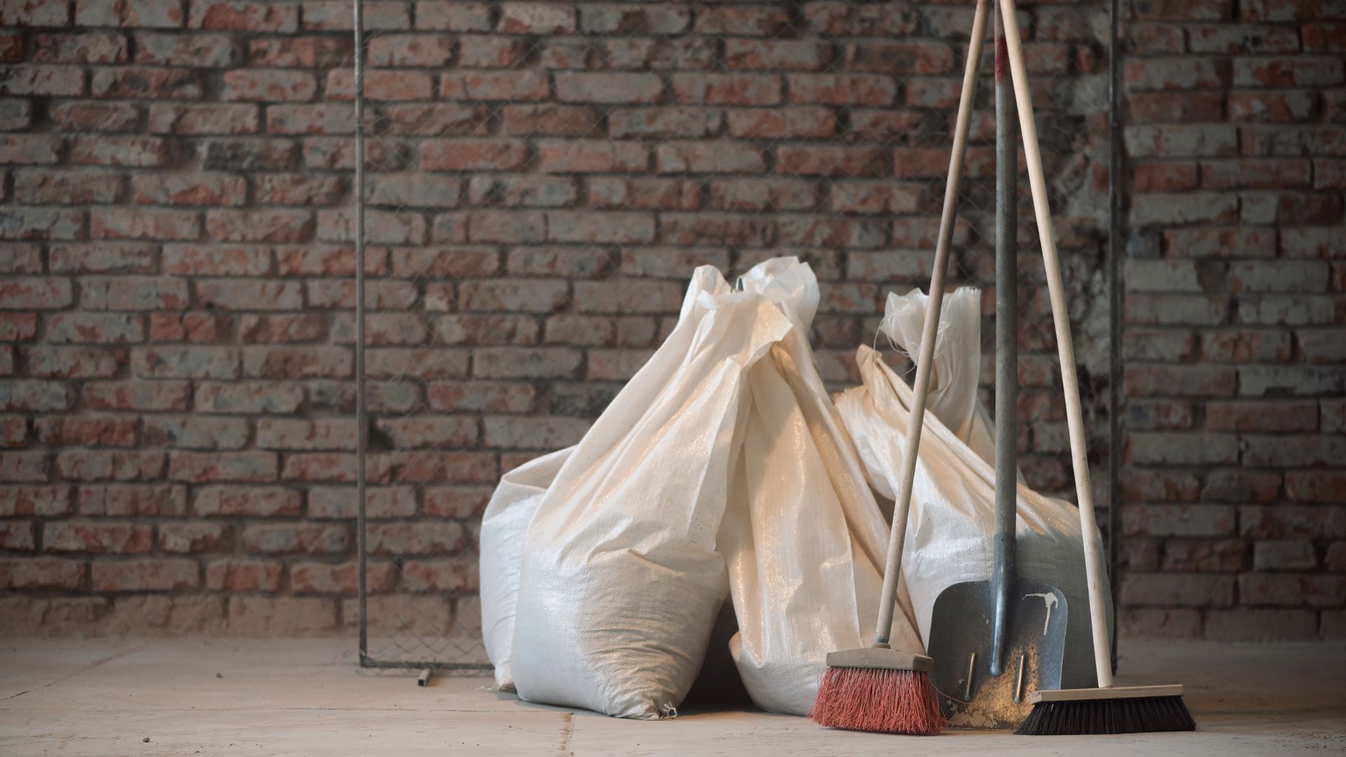 White bags, broom, and dustpan against a brick wall in a cleaning scene