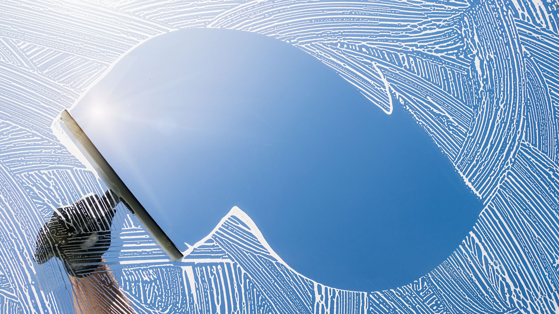 Squeegee cleaning blue-tinted window with intricate fingerprint-like background pattern