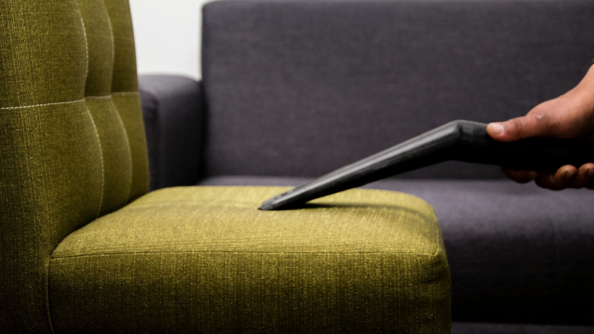 Hand holding remote control on green and gray sofa